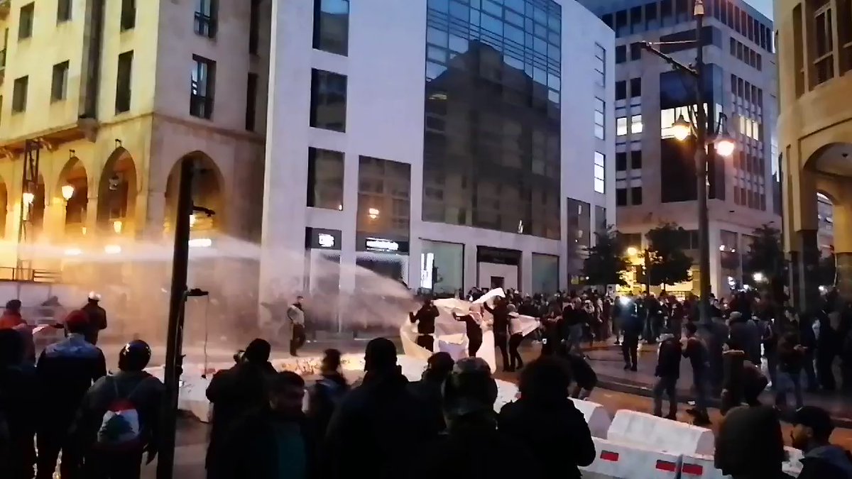 Protesters try to protect themselves with a white sheet from the water cannons near Lebanon Parliament